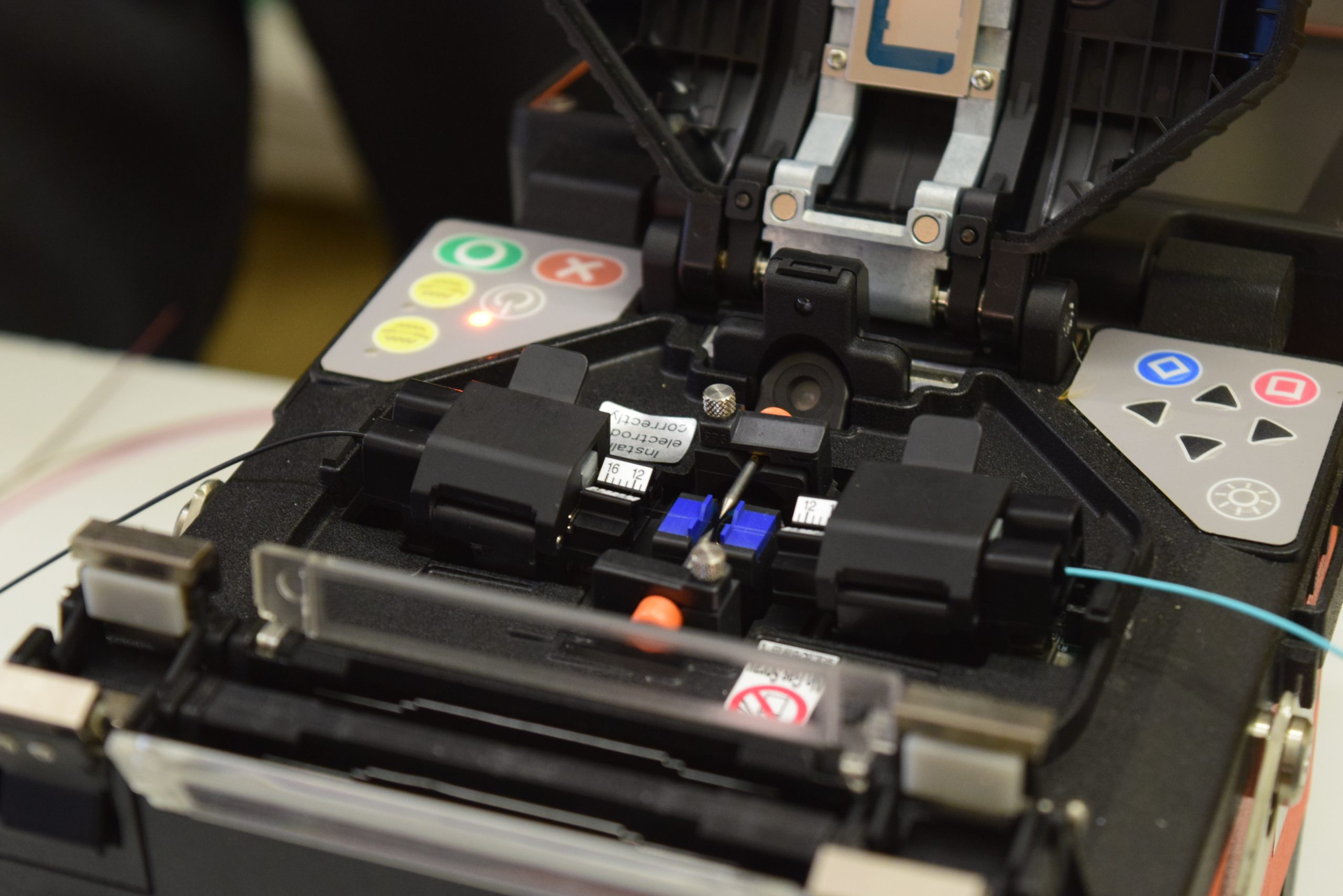 Close-up photo of fibers in a splicing machine, highlighting the precision and technical expertise involved in the fiber optic cable splicing process.