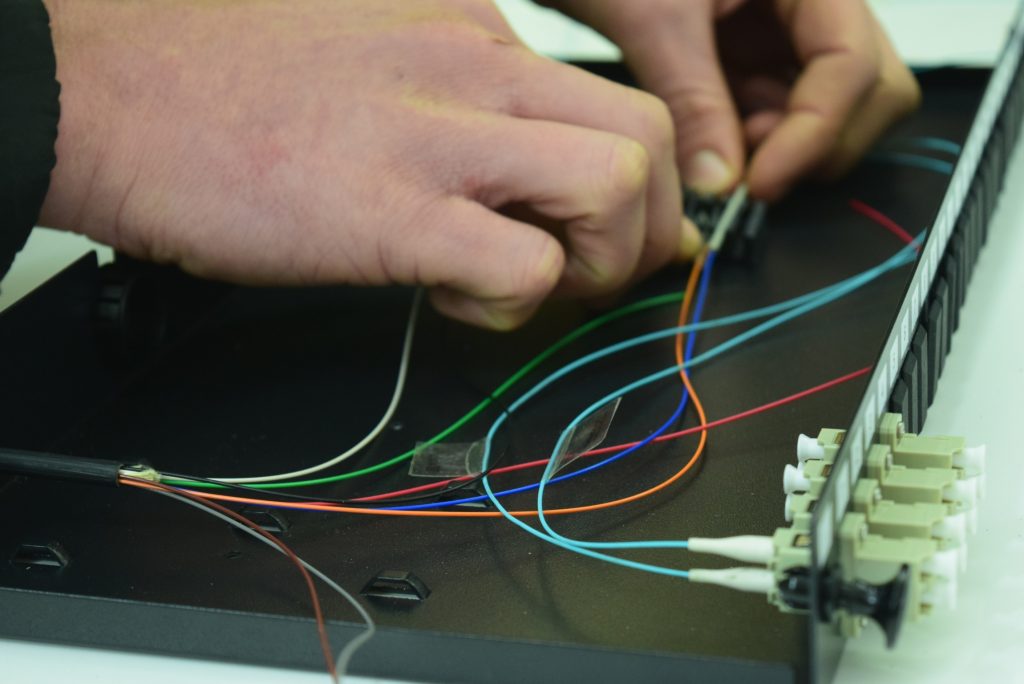 Close-up photo capturing the meticulous process of placing fibers into a tray, showcasing precise workmanship in fiber optic structured cabling network installation.