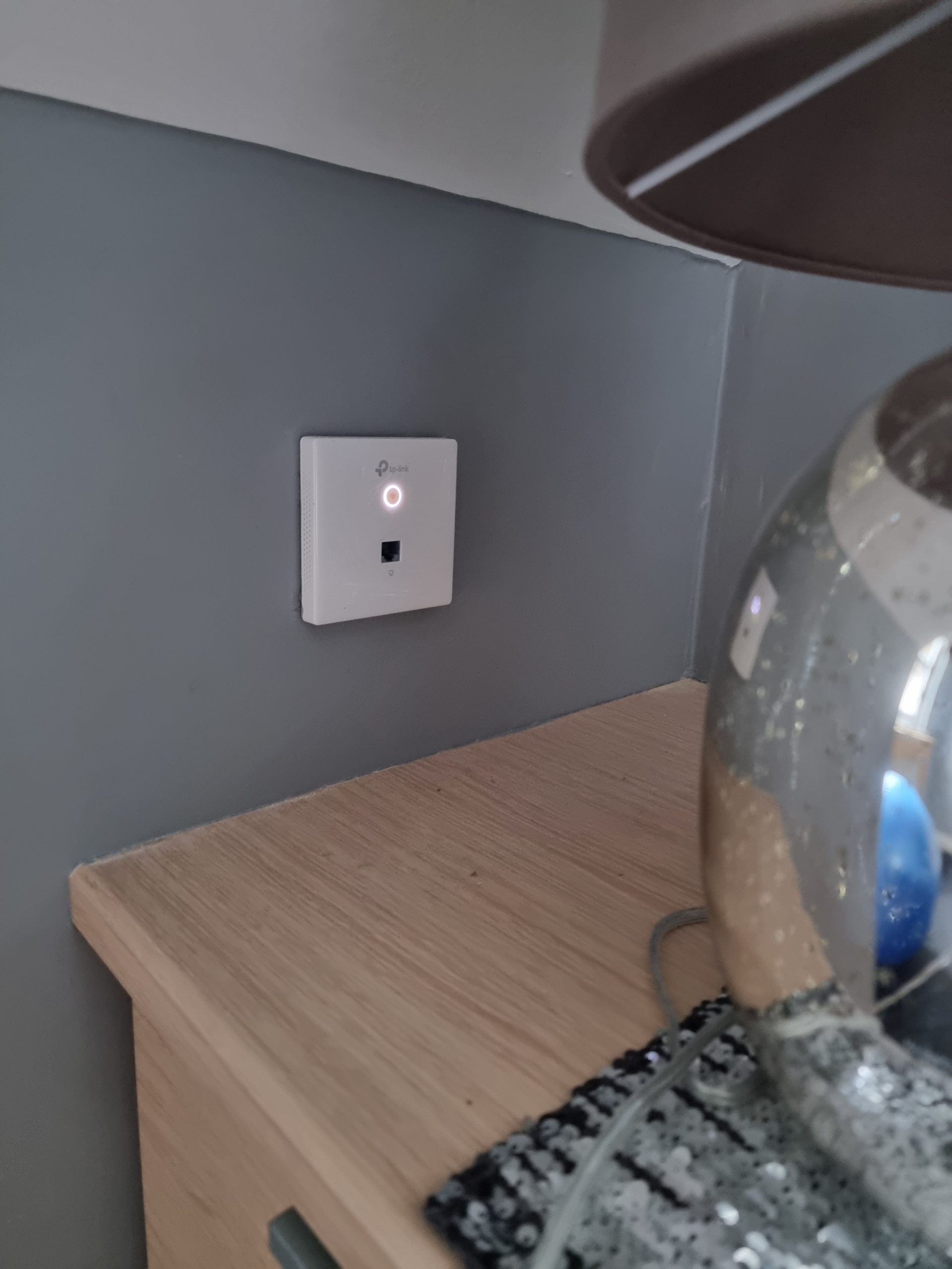 TP-Link WiFi installed in wall reflecting off metal lamp, blending technology seamlessly into the environment for enhanced connectivity.